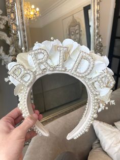 a person holding up a white bridal headpiece in front of a large mirror