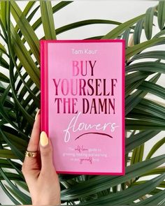 a person holding up a pink book with the title buy yourself the damn flowers