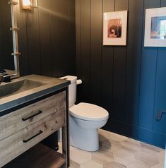 a white toilet sitting next to a bathroom sink under a mirror on top of a wooden cabinet