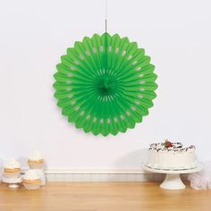 a cake and cupcakes on a table with a green fan hanging from the wall