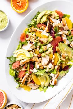 a white plate topped with a salad next to oranges and guacamole