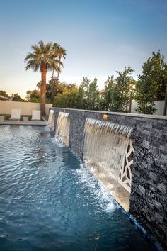 an outdoor swimming pool with water flowing from it's sides and palm trees in the background