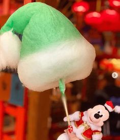 a green and white stuffed animal hanging from a string with other toys in the background