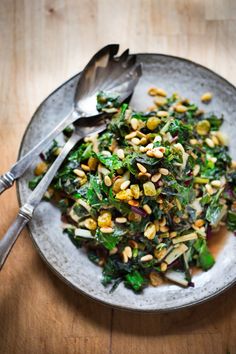 a white plate topped with greens and nuts next to two spoons on top of a wooden table