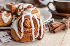 cinnamon buns with icing sitting on plates next to coffee cups and cinnamon sticks