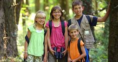 a group of young children standing next to each other on a forest floor with trees in the background