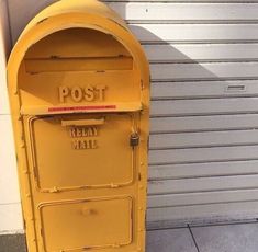 an old yellow mailbox sitting on the side of a building next to a garage