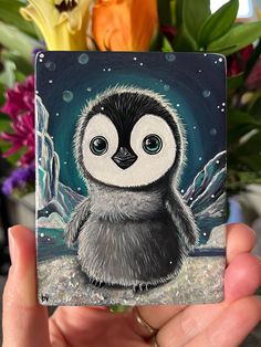 a hand holding up a small card with a penguin on it's face and wings