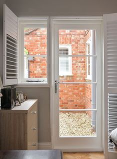 an open door leading to a bedroom with a brick wall and white shutters on the outside