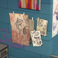 there are some drawings hanging on the wall next to each other in front of a blue brick wall