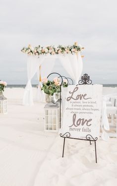 a sign that says love is in front of some chairs and flowers on the beach