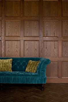 a blue couch sitting in front of a wooden paneled wall with two pillows on it