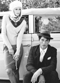 a man sitting on the back of a car next to a woman in a hat