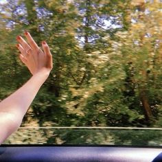 a person's hand out the window of a car with trees in the background