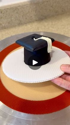 a hand holding a graduation cap on top of a cake plate with red and white stripes