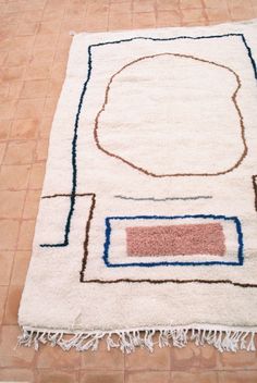 a white rug with blue and red designs on it in the middle of a tile floor