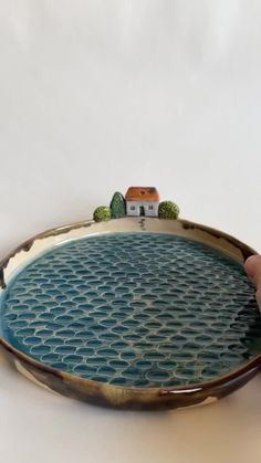 a person is holding a plate with a house on it and trees in the background