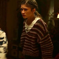 a woman standing in front of a mirror wearing a striped sweater and braided hair