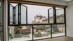 an open window shows the view of buildings and a castle in the distance, with a wooden floor