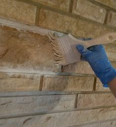 a person with blue gloves holding a white brush in their hand on a brick wall