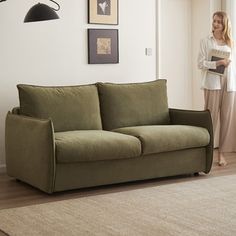 a woman standing next to a couch in a living room with a lamp on the wall