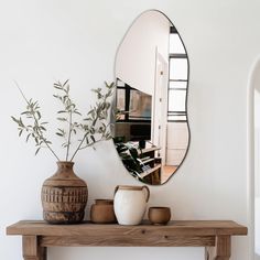 a mirror sitting on top of a wooden table next to a vase and potted plant