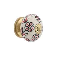 a white and red flowered cabinet knob with gold plated accents on the front