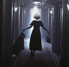 a woman in a black dress walking down a hallway with her hand on the ground