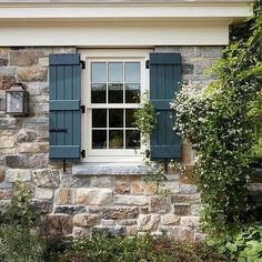 a stone house with blue shutters and white trim on the window sill is surrounded by greenery