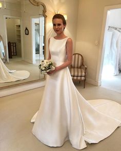 a woman in a white wedding dress standing next to a mirror and holding a bouquet