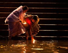 two people kneeling down in the water with a lit candle on their feet and hands