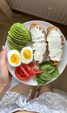 a person holding a plate with eggs, avocado and tomatoes on it in their hands