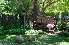 a wooden bench sitting in the middle of a lush green yard next to a tree