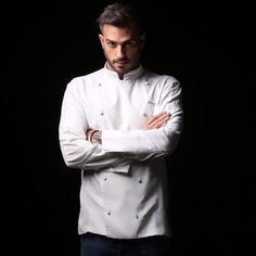 a man standing with his arms crossed wearing a white chef's coat and blue jeans