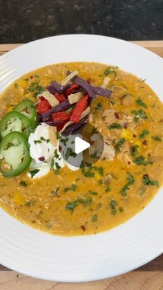 a white bowl filled with soup and vegetables on top of a wooden table next to a fork