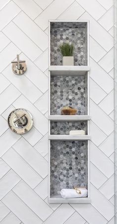 a bathroom with white and gray tile on the walls, shelving unit in the shower