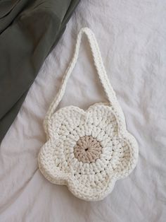 a white crocheted bag laying on top of a bed next to a pillow