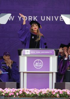 a woman standing at a podium with her arms in the air while wearing a graduation cap and gown