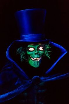 a man in a top hat and green face paint is wearing a blue caper