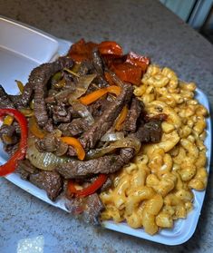 a white plate topped with pasta and meat next to macaroni on a counter