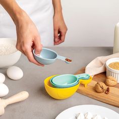 a person scooping food from a yellow bowl into a blue bowl on top of a wooden cutting board