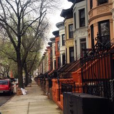 a row of houses on a city street with cars parked along the curb and trees lining the sidewalk