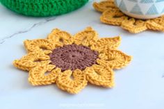 two crocheted flower coasters sitting on a table next to a coffee cup