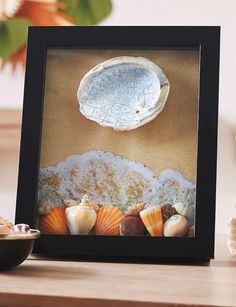 there is a picture frame with seashells on it and a bowl next to it