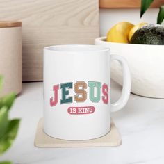 a white coffee mug sitting on top of a counter next to a bowl of fruit