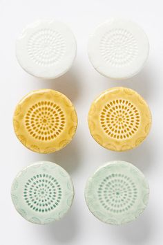 four ceramic dishes with holes in them on a white surface, one yellow and the other green