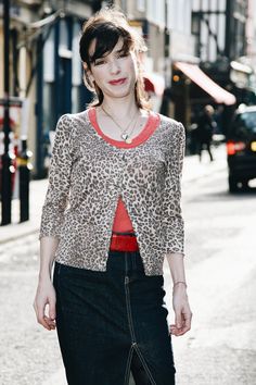 a woman walking down the street wearing a leopard print top and black pencil skirt with red accents