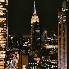 the empire building is lit up at night in new york city, ny with skyscrapers visible