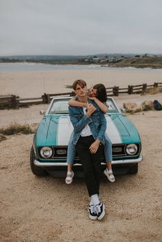 two people sitting on the hood of a car in front of a body of water