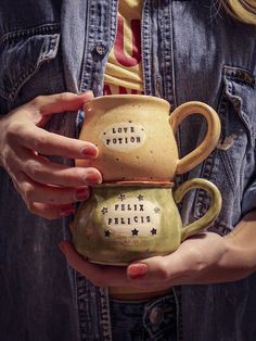 a woman holding two mugs with writing on them